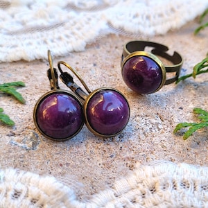May include: A set of purple gemstone jewelry featuring a ring and a pair of earrings. The ring and earrings have a bronze finish.
