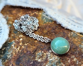 Op de afbeelding: Een zilveren ketting met een ronde hanger met een lichtgroene steen.