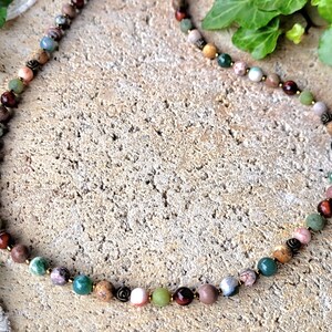 Peut inclure: Un collier de perles multicolores avec une vari&eacute;t&eacute; de pierres, notamment du vert, du brun, du rose et du rouge. Le collier est fait de pierres naturelles et est enfil&eacute; sur un cordon de couleur dor&eacute;e.