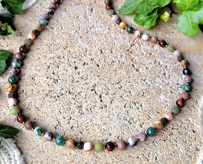Peut inclure: Un collier de perles multicolores avec une vari&eacute;t&eacute; de pierres, notamment du vert, du brun, du rose et du rouge. Le collier est fait de pierres naturelles et est enfil&eacute; sur un cordon de couleur dor&eacute;e.