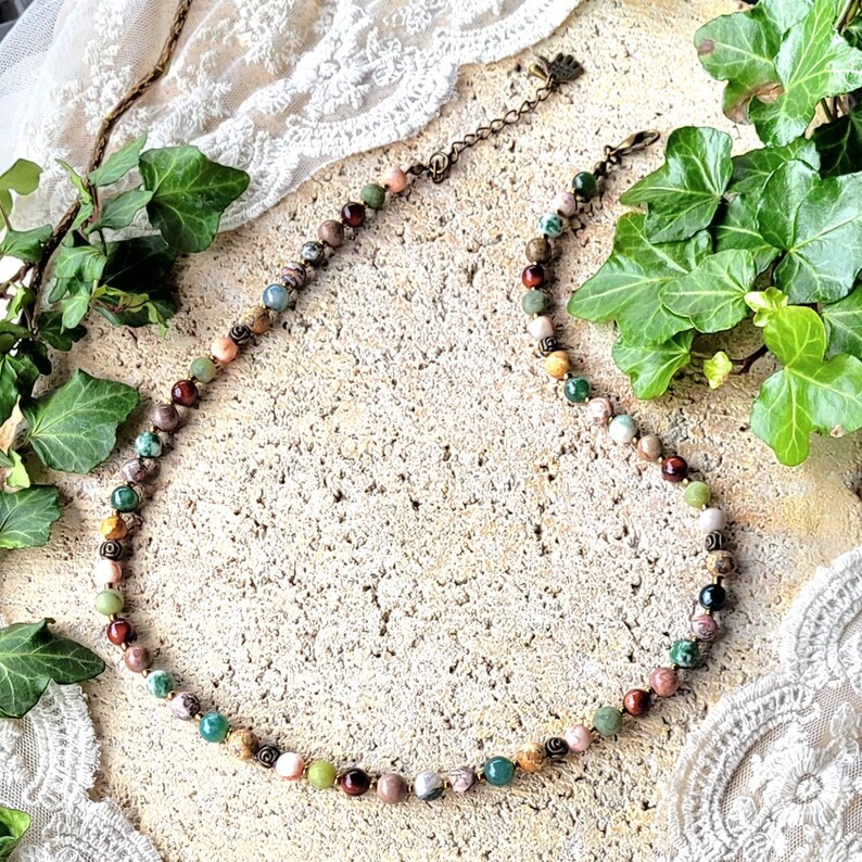 Peut inclure: Un collier de pierres pr&eacute;cieuses multicolores avec un fermoir en bronze. Le collier pr&eacute;sente une vari&eacute;t&eacute; de pierres, notamment du vert, du brun, du rose et du blanc.
