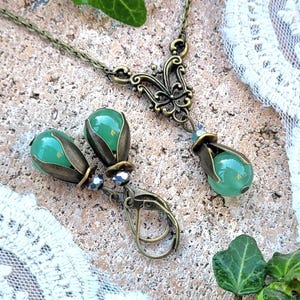 Pode incluir: Um colar com pingente de vidro verde e brincos combinando com um design de filigrana de bronze. O pingente apresenta um design de borboleta.