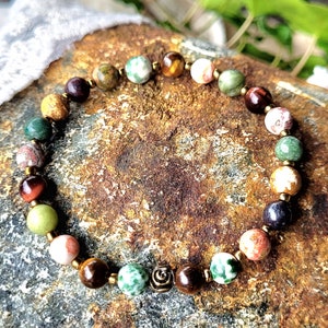 Peut inclure: Un bracelet en pierres pr&eacute;cieuses multicolores avec un charme en or. Le bracelet est compos&eacute; de perles d'&oelig;il de tigre, de jaspe, d'agate et d'autres pierres.