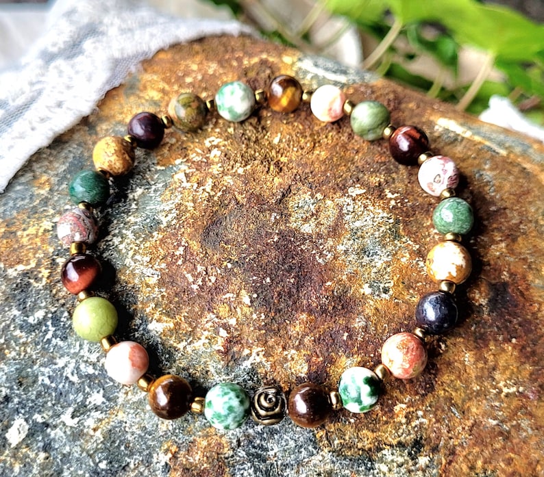 Peut inclure: Un bracelet en pierres pr&eacute;cieuses multicolores avec un charme en or. Le bracelet est compos&eacute; de perles d'&oelig;il de tigre, de jaspe, d'agate et d'autres pierres.