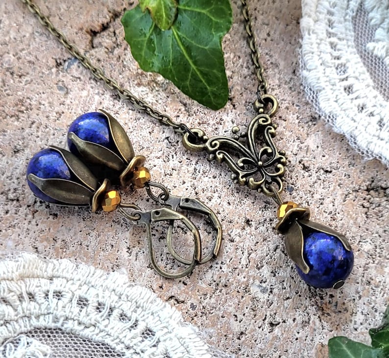 Pode incluir: Um par de brincos e um colar com pedras de l&aacute;pis-laz&uacute;li azuis engastadas em desenhos florais de bronze ornamentados. Os brincos t&ecirc;m um design de gota com um pequeno acento de contas douradas. O colar tem um pingente com um design de borboleta.