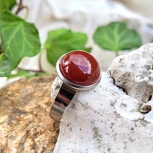 Op de afbeelding: Een zilveren ring met een rode carneol edelsteen. De ring is gezet in een bezel setting en heeft een gladde, gepolijste afwerking.