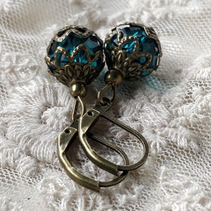 Pode incluir: Um par de brincos de vidro azul turquesa com filigrana de bronze ornamentada e fechos de alavanca.