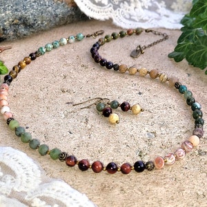 May include: A multi-colored gemstone necklace with matching earrings. The necklace features a variety of stones, including tiger's eye, red jasper, and green aventurine. The earrings are made with the same stones as the necklace.