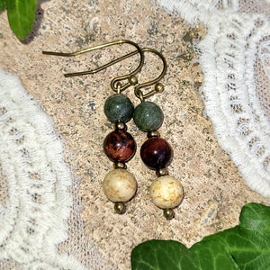 May include: A pair of earrings with three beads each. The top bead is green, the middle bead is red, and the bottom bead is cream colored.