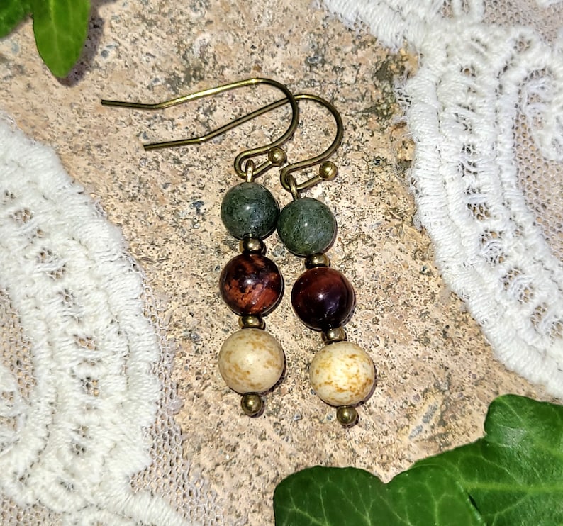May include: A pair of earrings with three beads each. The top bead is green, the middle bead is red, and the bottom bead is cream colored.