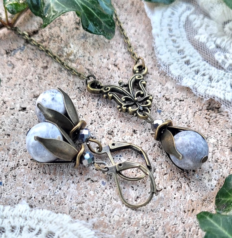 Pode incluir: Um conjunto de colar e brincos de prata e bronze com um design floral e contas de pedra cinza.