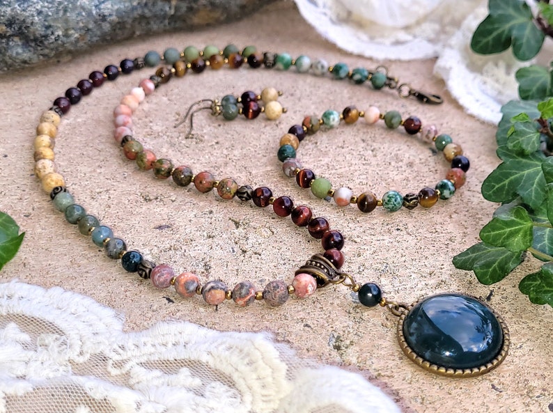 May include: A multi-colored gemstone necklace with a large green agate pendant. The necklace is made with various stones, including tiger's eye, jasper, and aventurine. The necklace is paired with a matching bracelet and earrings.