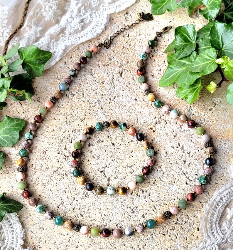 Peut inclure: Un ensemble de collier et de bracelet en pierres pr&eacute;cieuses multicolores. Le collier et le bracelet sont faits de diff&eacute;rentes pierres, notamment du vert, du brun, du rouge et du rose. Le collier a un fermoir en laiton.