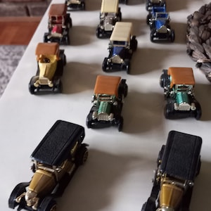 Peut inclure: Collection de modèles réduits de voitures anciennes de différentes couleurs, dont or, noir, bleu et vert. Les voitures ont des détails et sont disposées sur une surface blanche. Les voitures ont un design classique avec un toit décapotable.
