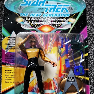 May include: A Star Trek: The Next Generation Geordi La Forge action figure in its original packaging. The figure is wearing a gold and black uniform and comes with accessories. The packaging features the Star Trek logo and text in English, French, and Spanish.