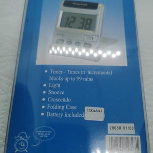 May include: A silver LCD alarm clock/timer with a digital display showing "12 38". Features include a snooze function, light, and folding case. The packaging lists timer functions up to 99 minutes. Battery included.