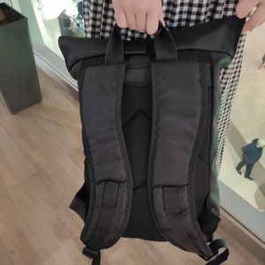 May include: Black backpack with a roll-top closure and adjustable straps. The backpack has a mesh back panel and a zippered pocket on the front.