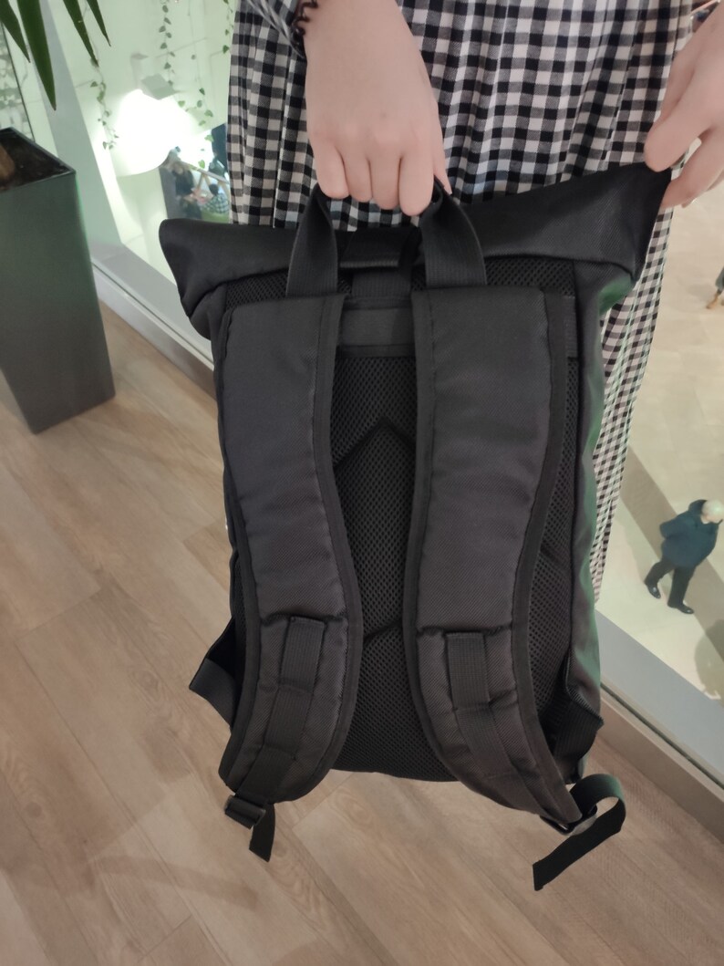May include: Black backpack with a roll-top closure and adjustable straps. The backpack has a mesh back panel and a zippered pocket on the front.