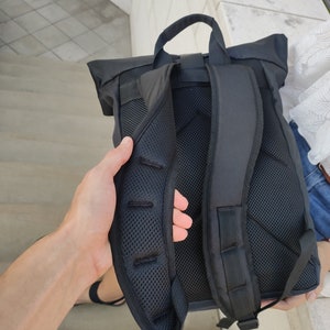 May include: Black backpack with a roll-top closure and adjustable straps. The backpack has a mesh back panel for ventilation.