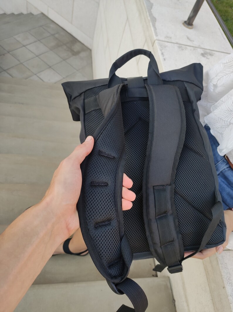 May include: Black backpack with a roll-top closure and adjustable straps. The backpack has a mesh back panel for ventilation.