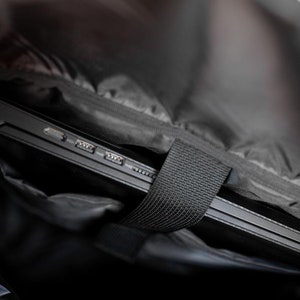 May include: A black laptop computer is inside a black backpack with a black strap. The laptop has several ports on the side.