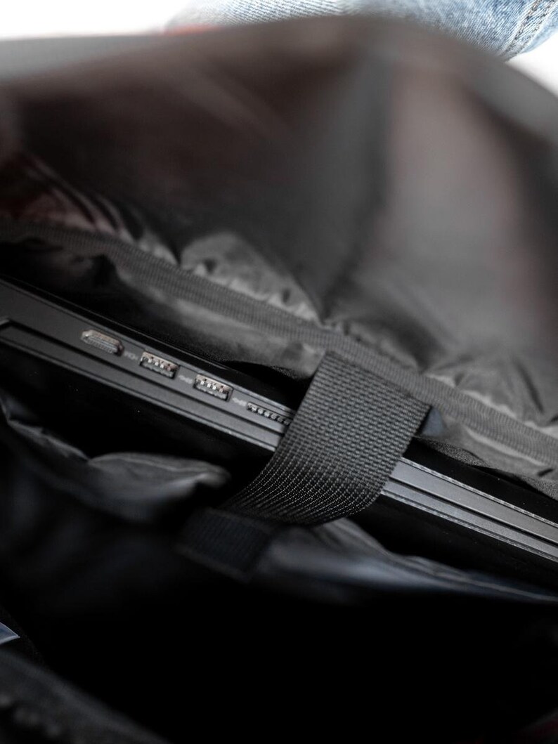 May include: A black laptop computer is inside a black backpack with a black strap. The laptop has several ports on the side.