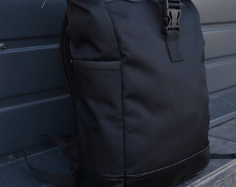 Pode incluir: Uma mochila preta de rolagem superior com fecho de fivela e guarnição de couro. A mochila é feita de um material durável e resistente à água.