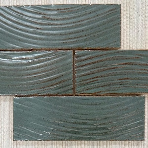 Op de afbeelding: Vier rechthoekige, teal-kleurige keramische tegels met een golvend, gestructureerd ontwerp. De tegels zijn in een kruispatroon gerangschikt en tonen hun glanzende afwerking en unieke oppervlakdetails. De randen hebben een bruine tint.