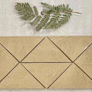 Puede incluir: Un conjunto de seis azulejos triangulares de cerámica beige con una superficie texturizada sutil. Los azulejos están dispuestos en un patrón para formar un triángulo más grande.