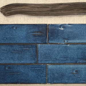 Puede incluir: Seis baldosas de cerámica azules rectangulares con una superficie texturizada y bordes oscuros están dispuestas en forma de ladrillo. Encima de las baldosas hay un trozo de madera flotante. El fondo es beige y tejido.