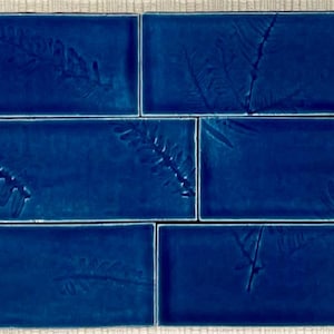 Pode incluir: Seis azulejos retangulares, brilhantes, azul escuro, dispostos em duas filas. Cada azulejo apresenta um desenho de samambaia em relevo. Os azulejos são de um azul rico e saturado, e os detalhes da samambaia adicionam um elemento natural e texturizado.