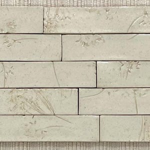 Op de afbeelding: Een set van zes off-white keramische tegels met een subtiel reliëfpatroon van bloemen. De tegels zijn in een verspringende opstelling geplaatst, waardoor een visueel aantrekkelijk en getextureerd oppervlak ontstaat.