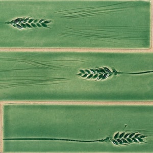 May include: Three green ceramic tiles with a raised design of wheat stalks. The tiles are arranged in a vertical stack.