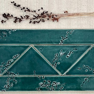 May include: A set of teal green ceramic tiles with a floral pattern. The tiles are arranged in a staggered pattern, with the rectangular tiles on top and the triangular tiles below.