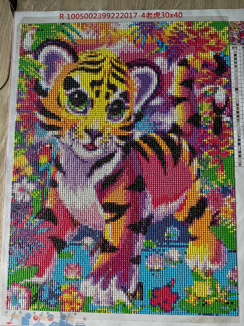 May include: A colorful diamond painting of a tiger cub. The artwork features a vibrant mix of colors, including yellow, orange, pink, purple, and blue. The tiger cub is the central focus, surrounded by a floral background. The dimensions are 30x40 cm.