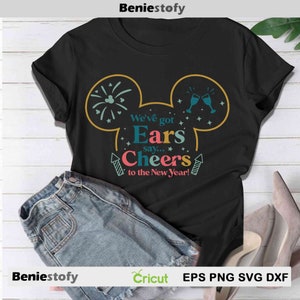 May include: Black t-shirt with a festive design featuring Mickey Mouse ears, fireworks, and champagne glasses. The text reads "We've got Ears say... Cheers to the New Year!" A pair of denim shorts and high heels are also in the image.