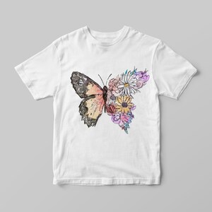 May include: White t-shirt with a colorful butterfly and floral design. The butterfly is outlined in black and has pink, orange, and yellow wings. The flowers are pink, yellow, and purple.
