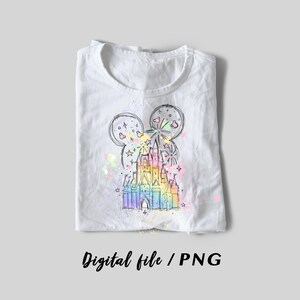May include: A white t-shirt with a rainbow-colored sketch of a castle with Mickey Mouse ears and fireworks. The design is on a white t-shirt with a subtle splatter effect.