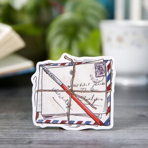May include: A stack of vintage-style envelopes tied with twine and a red pen, with a blue and red striped pattern on the edges. The envelopes have handwritten text and a stamp.