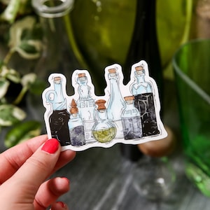 May include: A sticker featuring a collection of illustrated potion bottles with cork stoppers. The bottles are in various shapes and sizes, with shades of blue, green, and black. The sticker has a white border and is held by a hand.
