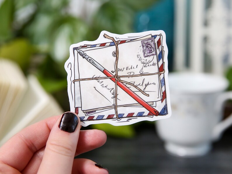 May include: A sticker of a stack of vintage envelopes tied with twine and a red pen. The envelopes have handwritten text and a blue and red stamp.