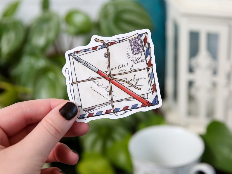 May include: A sticker of a stack of envelopes tied with twine and a red pen. The envelopes have handwritten text and a blue and red stamp.