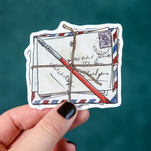 May include: A sticker of a stack of envelopes tied together with twine and a red and black pen. The envelopes have a blue and red striped pattern and are addressed with handwritten text.
