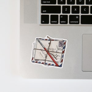 May include: A sticker of a stack of envelopes tied with twine and a red pen. The envelopes are decorated with a blue and red striped pattern and have handwritten text.