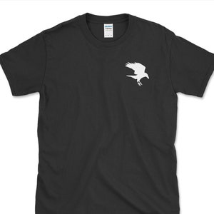 May include: Black t-shirt featuring a white silhouette of a bird in flight. The bird design is on the upper left chest area of the shirt. The shirt is a crew neck style and appears to be made of cotton.