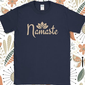 K&ouml;nnte beinhalten: Marineblaues T-Shirt mit dem Wort "Namaste" in beigefarbener Schrift, dar&uuml;ber eine Lotusblume. Das T-Shirt hat einen Rundhalsausschnitt und kurze &Auml;rmel. Der Hintergrund ist ein Blumenmuster mit Blumen und Schmetterlingen.