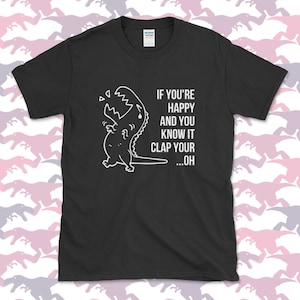 Peut inclure: T-shirt noir avec un dinosaure de dessin anim&eacute; blanc et le texte "Si tu es heureux et que tu le sais, applaudis...oh".