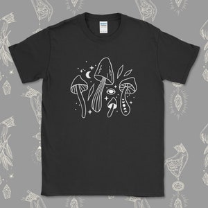 Könnte beinhalten: Schwarzes T-Shirt mit einem weißen Umriss von Pilzen, Sternen, einem Halbmond und einem Auge. Der Text "Shroom Queens" ist auf dem Shirt geschrieben.