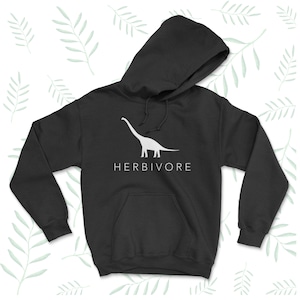 Op de afbeelding: Zwarte hoodie met een wit silhouet van een dinosaurus en de tekst "HERBIVORE" gedrukt op de voorkant.