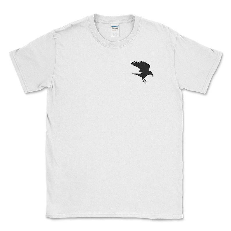 May include: White t-shirt with a black raven silhouette on the upper left chest. The raven is depicted in mid-flight, with its wings spread. The shirt is made of a soft material and has a crew neck.